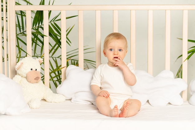 Junge Blondine mit blauen Augen in einem weißen Body auf einem Bett mit Baumwollunterwäsche zu Hause vor dem Zubettgehen