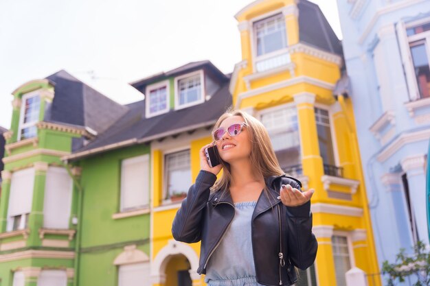 Junge Blondine mit Lederjacke telefoniert hinter bunter Fassade