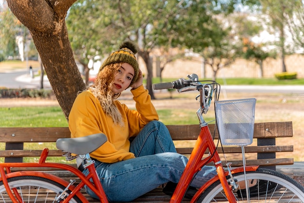 Junge Blondine sitzt auf einer Bank und ruht sich mit ihrem Fahrrad im Park aus