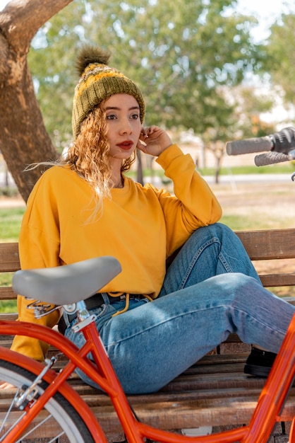 Junge Blondine sitzt auf einer Bank und ruht sich mit ihrem Fahrrad im Park aus