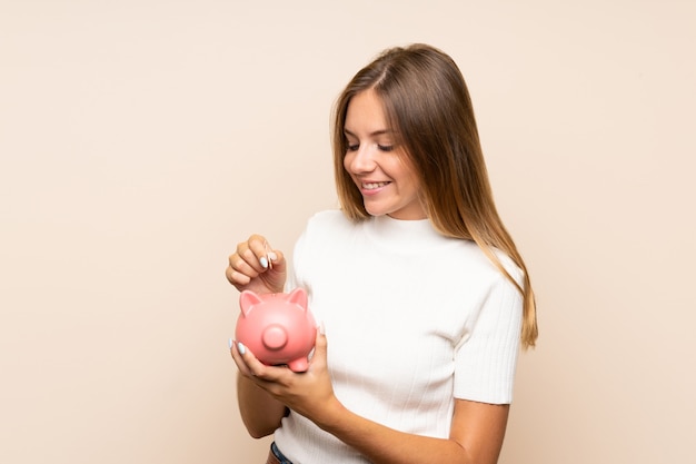 Junge Blondine über dem lokalisierten Hintergrund, der ein großes Sparschwein hält