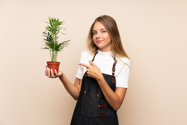 Junge Blondine über der lokalisierten Wand, die einen Blumentopf nimmt und ihn zeigt