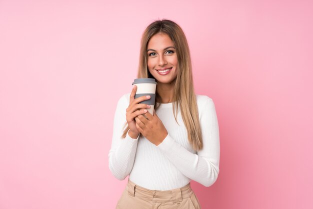 Junge Blondine über lokalisiertem rosa haltenem Kaffee zum Mitnehmen