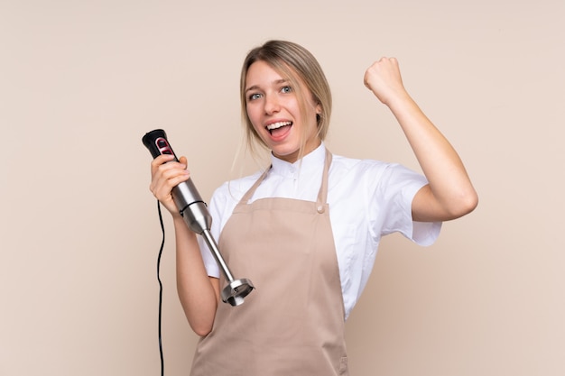 Junge Blondine, welche die Mischmaschine feiert einen Sieg verwenden