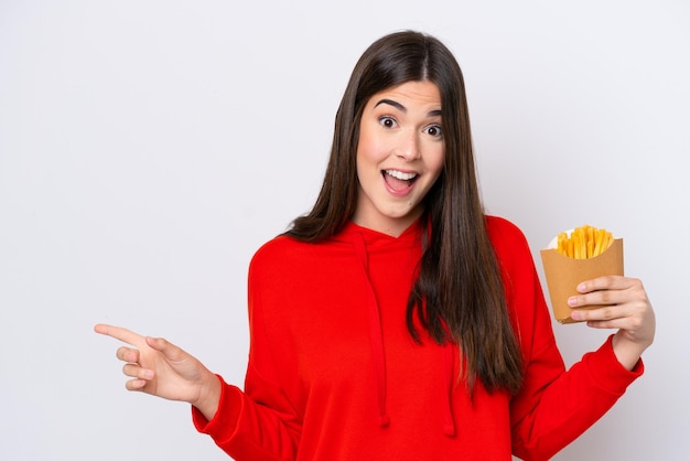 Junge Brasilianerin fängt Pommes frites isoliert auf weißem Hintergrund überrascht und zeigt mit dem Finger zur Seite