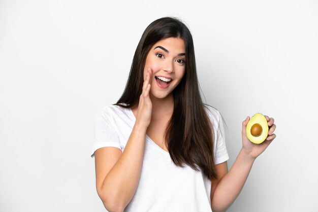 Junge Brasilianerin hält eine Avocado isoliert auf weißem Hintergrund und schreit mit weit geöffnetem Mund