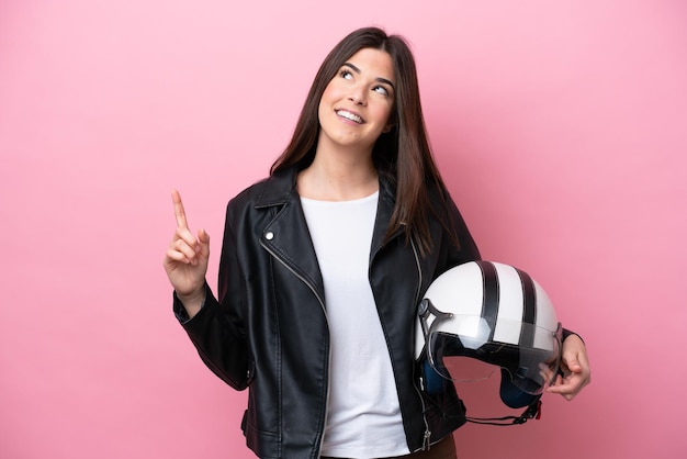 Junge Brasilianerin mit einem Motorradhelm isoliert auf rosa Hintergrund, der auf eine großartige Idee zeigt