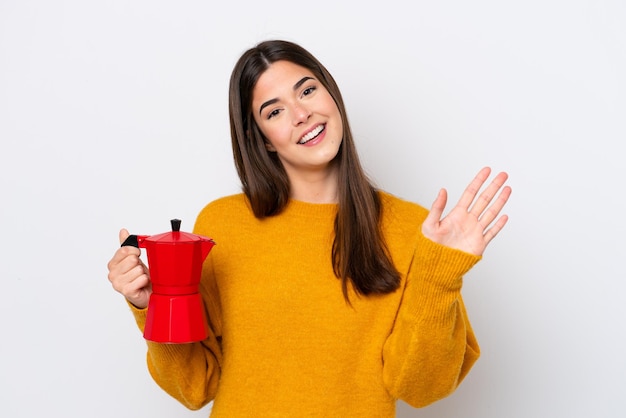 Junge Brasilianerin mit Kaffeekanne isoliert auf weißem Hintergrund salutiert mit der Hand mit glücklichem Ausdruck