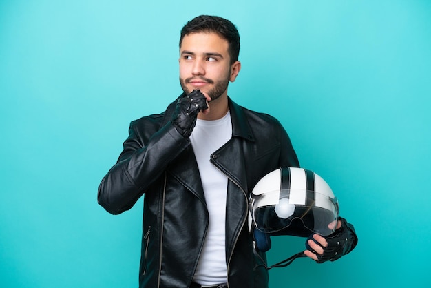 Junge Brasilianerin mit Motorradhelm isoliert auf blauem Hintergrund und nach oben schauend