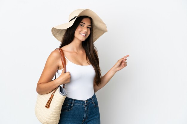 Junge Brasilianerin mit Pamela hält eine Strandtasche isoliert auf weißem Hintergrund und zeigt mit dem Finger zur Seite