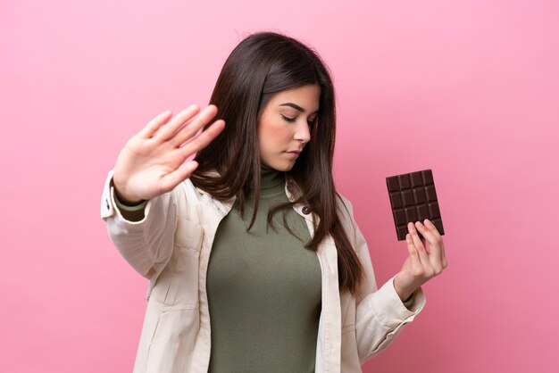 Junge Brasilianerin mit Schokolade isoliert auf rosa Hintergrund, Stoppgeste machend und enttäuscht