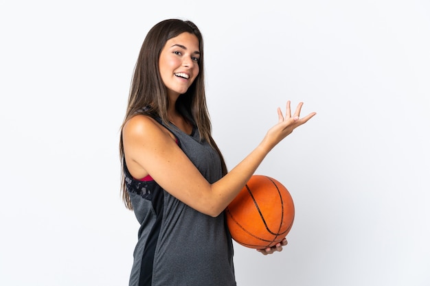 Junge brasilianische Frau, die Basketball spielt, lokalisiert auf weißer Wand, die Hände zur Seite für Einladung zum Kommen ausdehnt