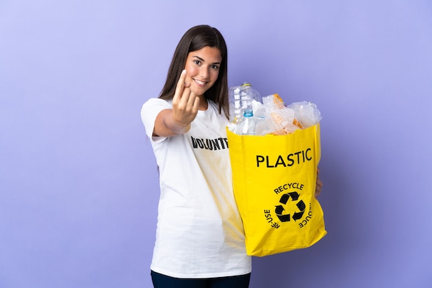 Junge brasilianische Frau, die eine Tasche voller Plastikflaschen hält, um lokalisiert auf lila zu tun, die kommende Geste tun