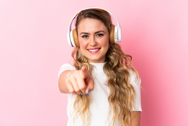 Junge brasilianische Frau isoliert auf rosa hörende Musik und zeigt nach vorne