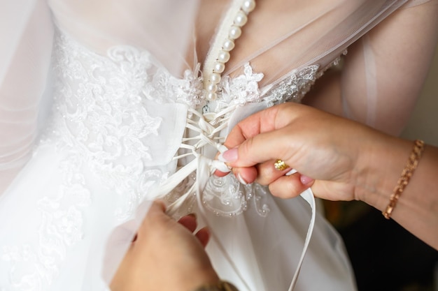 Junge Braut im Hochzeitskleid wartet auf die Freundin des Bräutigams, die hilft, ein Kleid zu befestigen