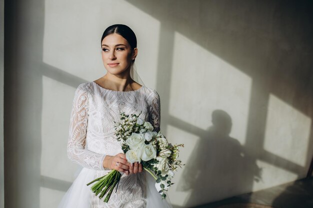 Junge Braut im weißen Hochzeitskleid, das Blumenstrauß hält und zu Hause wegschaut