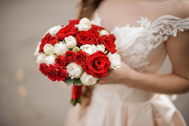 Junge Braut in einem Hochzeitskleid, das einen Blumenstrauß der eleganten weißen und roten Rosen hält