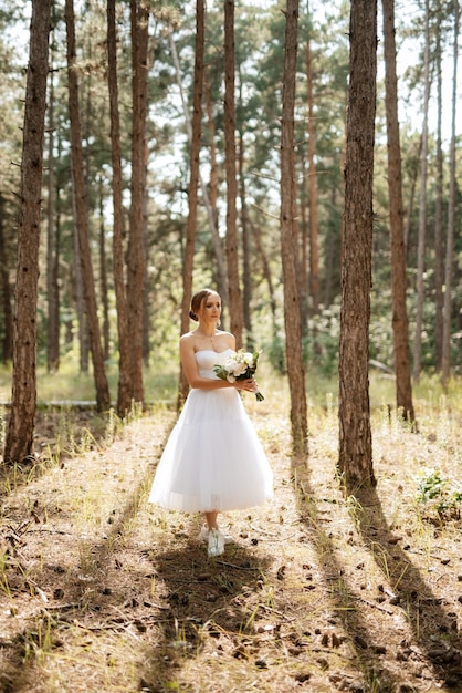 Junge Braut in einem weißen kurzen Kleid in einem Frühlingskiefernwald