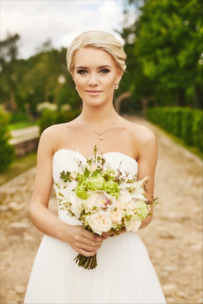 Junge Braut, schöne Blondine, Modellmädchen mit blauen Augen mit Blumen in den Händen, draußen