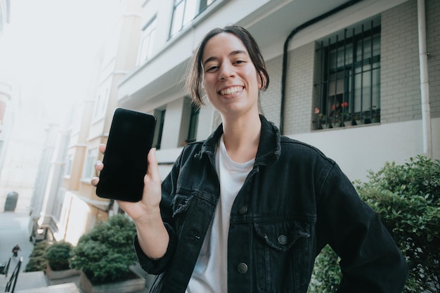 Junge, breit lächelnde Frau an einem sonnigen Tag mit SmartphoneGute StimmungModerner Technologiekopierraum