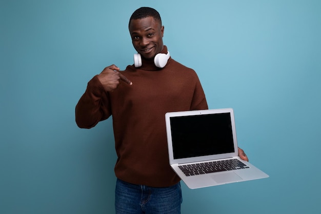 Junge brünette afrikanische Mann mit funktionierendem Laptop studiert auf dem Hintergrund mit Kopierraum