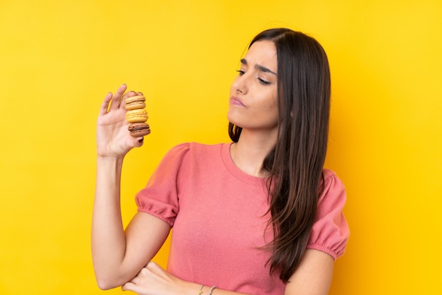 Junge brünette Frau, die bunte französische Macarons mit traurigem Ausdruck hält