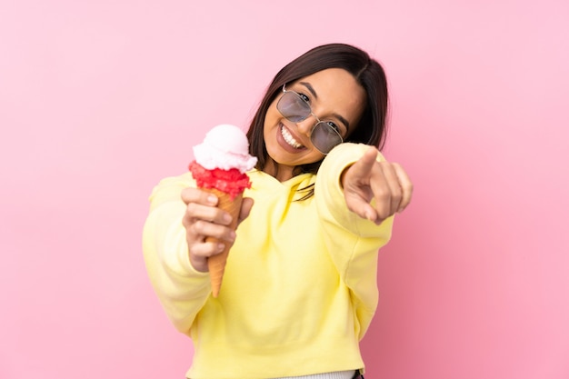 Foto junge brünette frau, die ein kornett-eis hält, zeigt finger auf sie beim lächeln