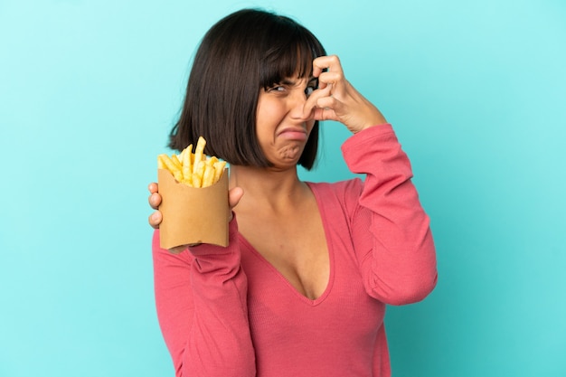 Junge brünette Frau, die gebratene Chips über isoliertem blauem Hintergrund hält holding