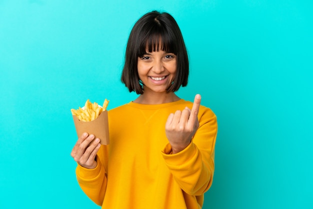 Junge brünette Frau, die gebratene Chips über isoliertem blauem Hintergrund hält und kommende Geste macht