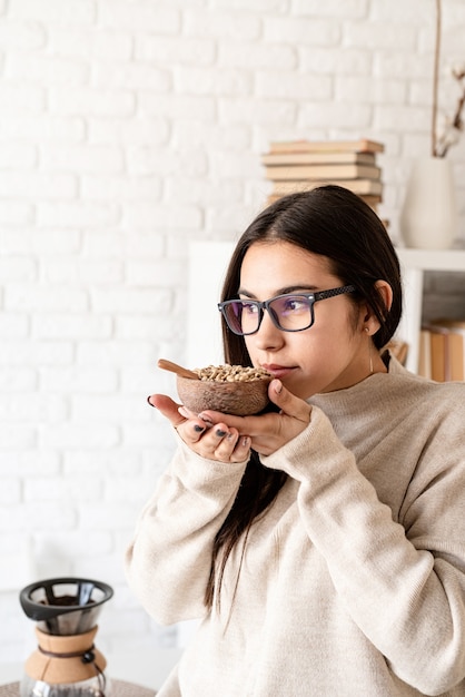 junge brünette Frau, die Kaffee in Kaffeemaschine braut und grüne Kaffeebohnen riecht