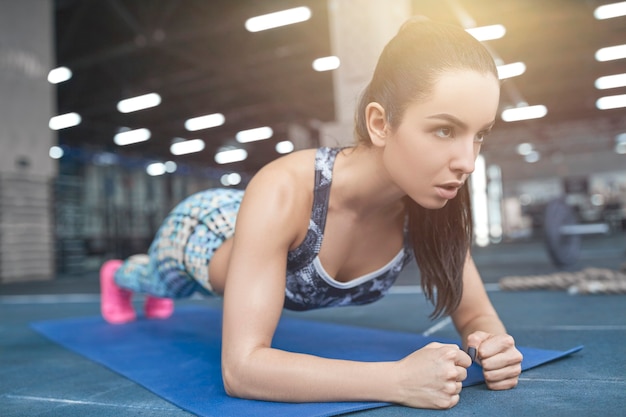 Junge brünette Frau, die Plank-Übungen in den Armen des Fitnessstudios und der Entwicklung der Rückenkraft macht