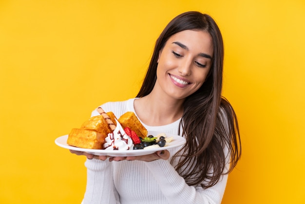 Junge brünette Frau, die Waffeln über isolierter Wand hält