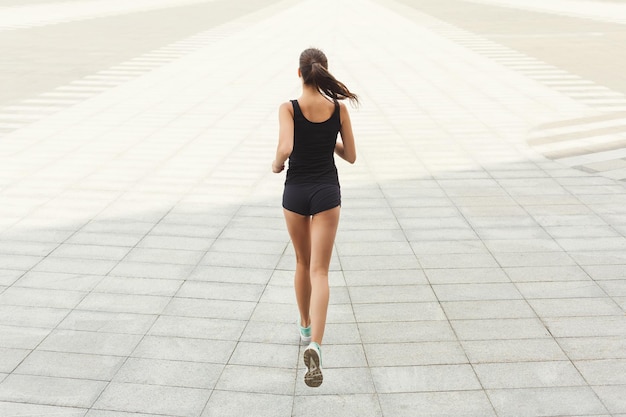 Junge brünette Frau läuft im Stadtzentrum, trainiert vor dem Marathon, Rückansicht, Kopierraum