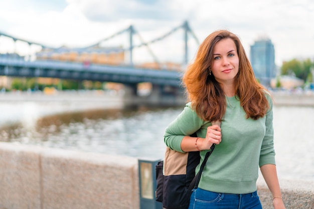 junge brünette Frau mit einem Rucksack geht entlang der Böschung in Moskau