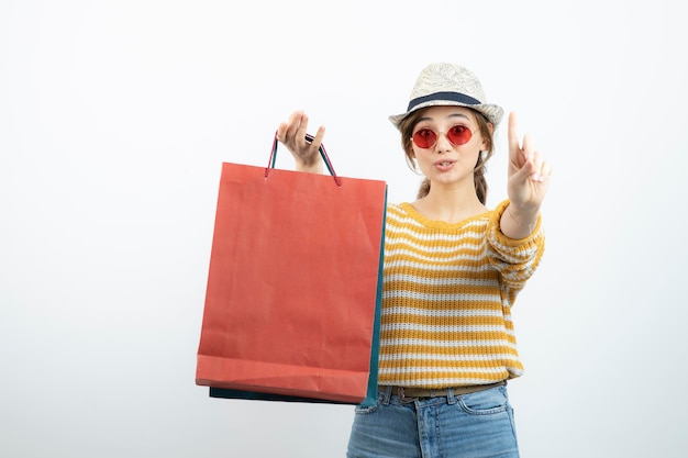 Junge brünette Frau mit Sonnenbrille, die Einkaufstüten hält und nach oben zeigt. Foto in hoher Qualität
