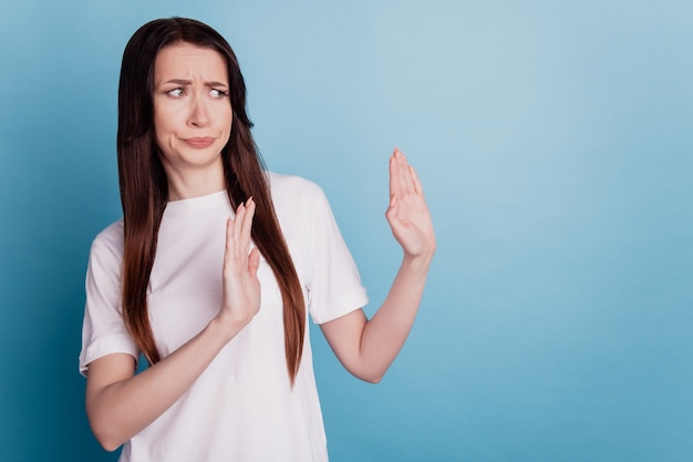 Junge brünette Frau trägt ein lässiges weißes T-Shirt über blauem Hintergrund und hat einen angewiderten Ausdruck