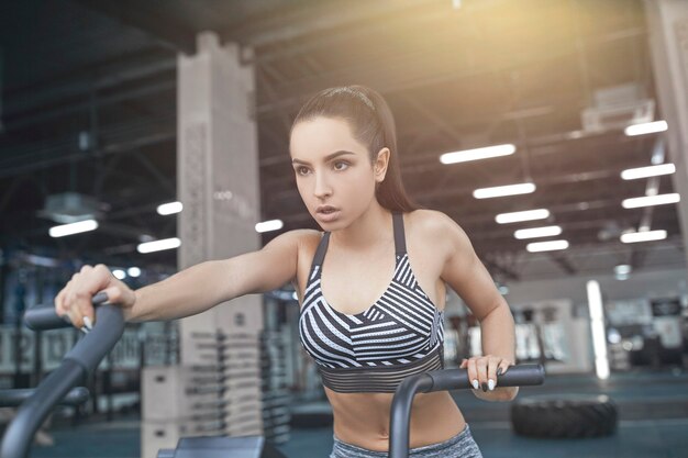 Junge brünette Frau trainiert im Fitnessstudio intensives Cardio-Training auf dem Fahrrad und freut sich