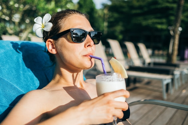 Junge brünette fröhliche Frau, die nahe Hotelschwimmbad bräunt