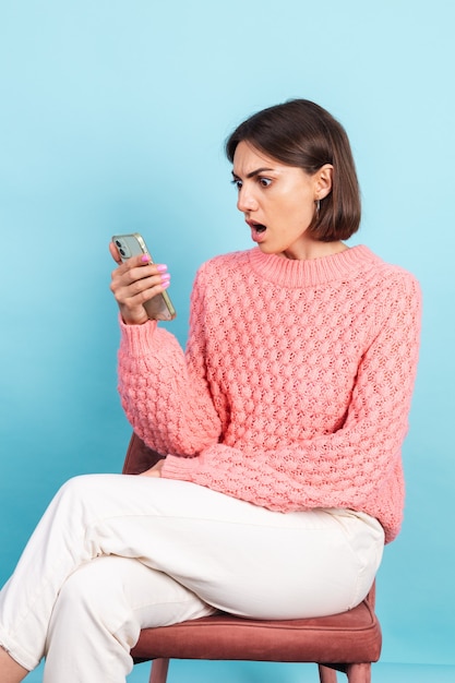 Junge Brünette im warmen rosa Pullover lokalisiert auf blauer Wand