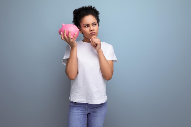 Junge brünette lateinamerikanische Frau in einem weißen T-Shirt sammelte Geld in einem Sparschwein