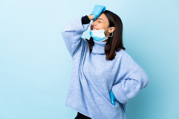 Junge brünette Mischlinge Frau, die mit einer Maske und Handschuhen über der isolierten blauen Wand vor dem Coronavirus schützt, hat etwas erkannt und beabsichtigt die Lösung