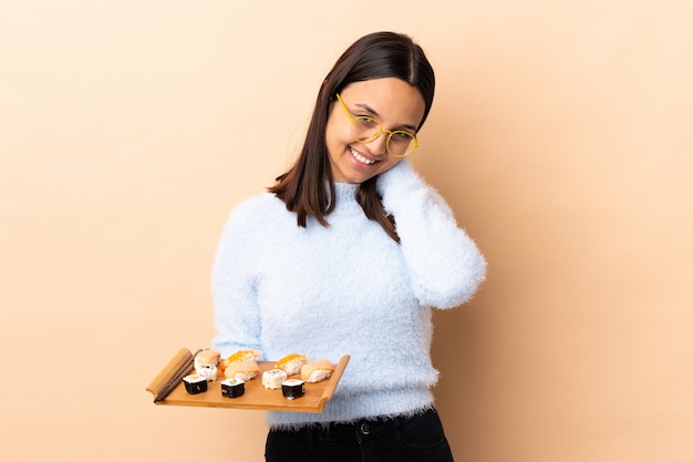 Junge brünette Mischrassenfrau, die Sushi über isoliertem Lachen hält