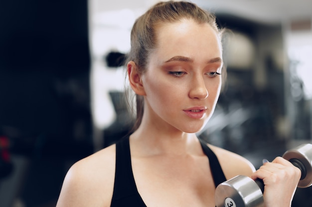 Junge brünette sportliche Frau, die mit Hantel in einem Fitnessstudio trainiert