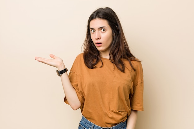 Junge Brunettefrau auf Beige beeindruckte das Halten des Kopienraumes auf Palme.