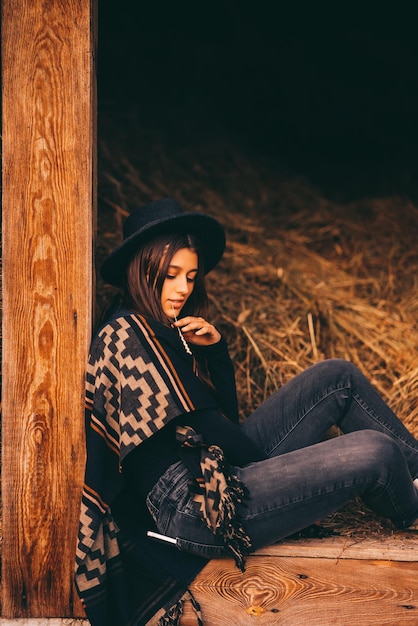 Junge Brunettefrau, die an der Scheune im Landhausstil sitzt