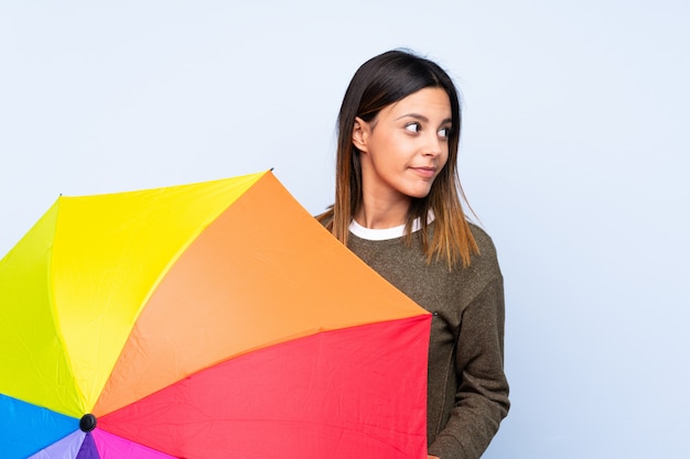 Junge Brunettefrau, die einen Regenschirm über blauer Wand hält