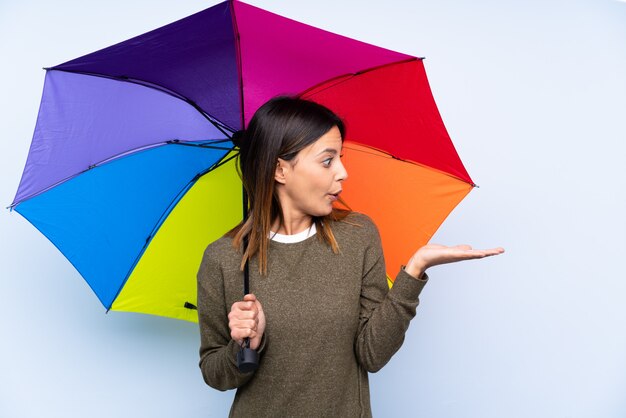 Junge Brunettefrau, die einen Regenschirm über der blauen Wand hält copyspace eingebildet auf der Palme hält