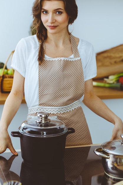 Junge Brunettefrau, die Suppe in der Küche kocht. Hausfrau, die hölzernen Löffel in ihrer Hand hält. Lebensmittel- und Gesundheitskonzept.