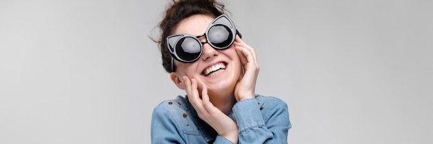 Junge Brunettefrau in den schwarzen Gläsern. Katzengläser. Die Haare sind zu einem Brötchen zusammengefasst. Die Frau hält ihr Gesicht.