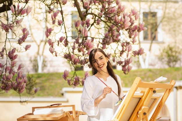 Junge Brunettekünstlerin, die in den Händen eine Bürste und eine Palette hält.